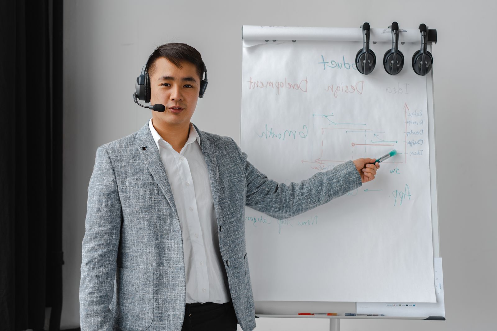 Contact center trainer wearing a headset leading a new-hire training session at a flipchart, with agent headsets hanging ready beside it
